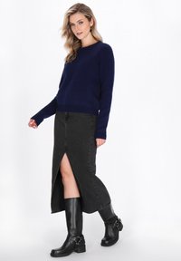 Pulover tricotat bleumarin, fustă din denim negru cu desfăcut frontal și cizme negre până la genunchi cu accente din catarame. Textură netedă și design ajustat.