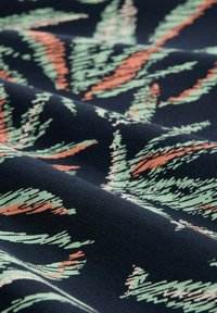 Textiel met een marineblauwe achtergrond en abstracte bladerenpatronen in groen en koraal. De stof heeft een gestructureerd oppervlak, ideaal voor meubelbekleding.