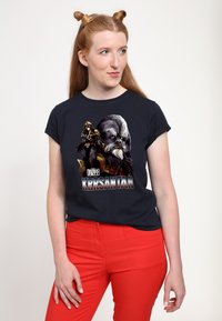 Czarna koszulka z grafiką postaci o szarej sierści na twarzy i zbroi, napis brzmi "Boba Fett Krrsantan". W zestawie z czerwonymi spodniami.