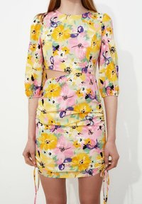 Blommig klänning med ett mönster i gult, rosa och lila, med puffärmar och passa skärning, accentuerad med justerbara dragsnören vid nederkanten.