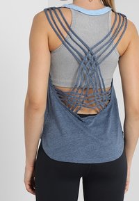 Blå linne med meshbak och korskorsade remmar, lager på lager över en grå ribbad linne. Mjuk textur och avslappnad passform.