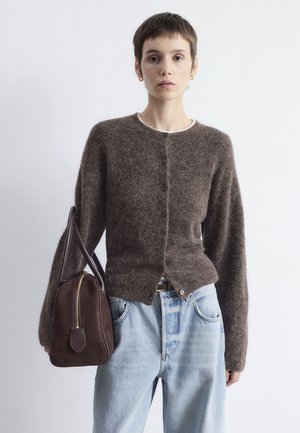 Brown, fluffy cardigan with round neckline and button closure, paired with light blue jeans. Person holds a dark brown shoulder bag.