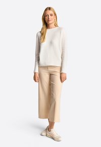 Lätt krämfärgad tröja med en lös passform, kombinerad med avslappnade beige beskurna byxor och beige sneakers. Texturen verkar mjuk och mysig.