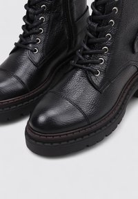 Bottines en cuir noir avec une finition texturée, bout rond, design à lacets, œillets en argent et semelle en caoutchouc épaisse avec des détails cousus.