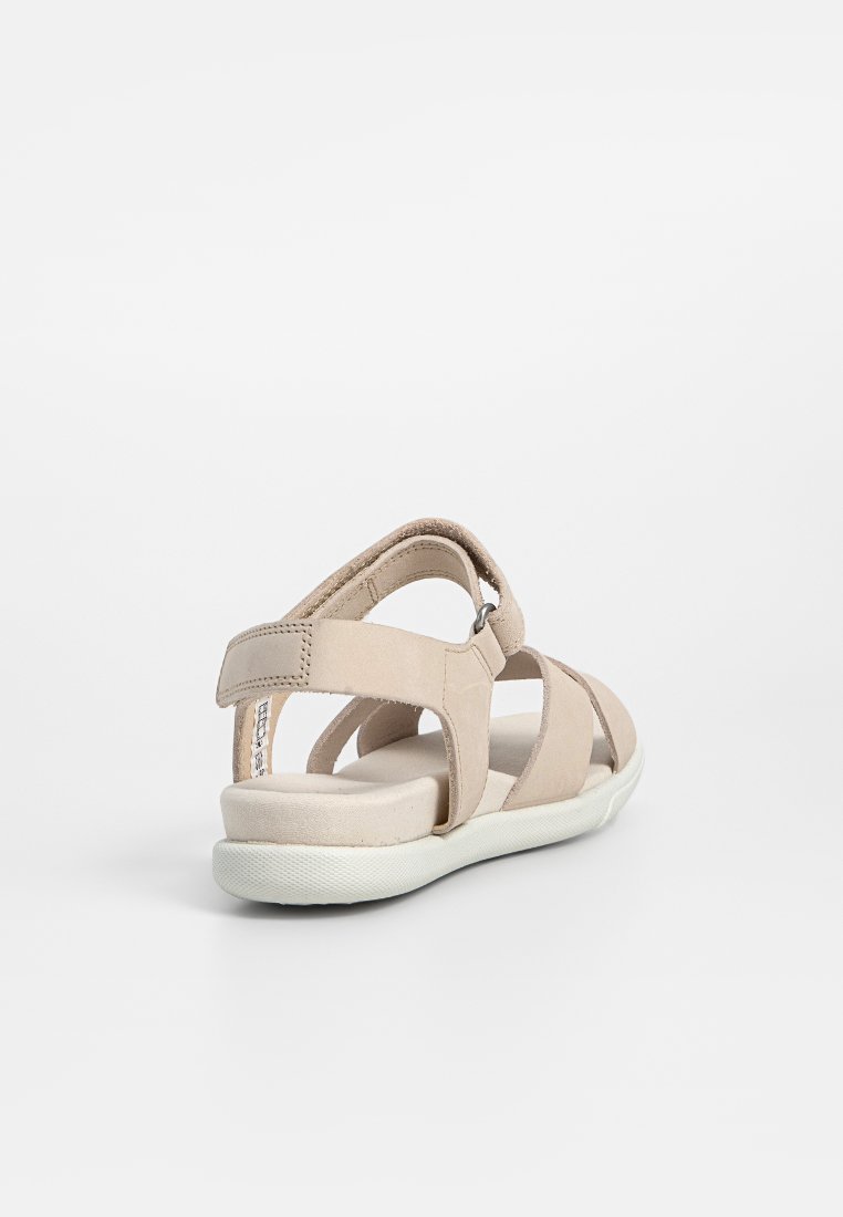 Beige Sandale mit einer samtartigen Textur, ausgestattet mit überkreuzten Riemen und verstellbarer Knöchelunterstützung. Die Sohle ist weiß und gepolstert für zusätzlichen Komfort.