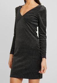 Svart klänning med långa ärmar, V-ringning, gjord av mjukt tyg med ett mönster av vertikala vita linjer. Slät textur och åtsittande silhuett.