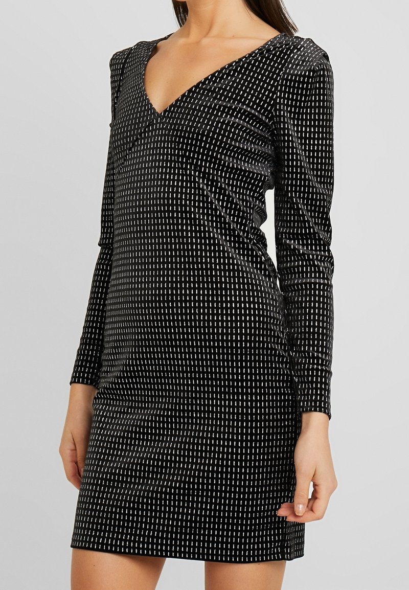 Svart klänning med långa ärmar, V-ringning, gjord av mjukt tyg med ett mönster av vertikala vita linjer. Slät textur och åtsittande silhuett.