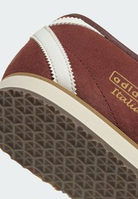 Καφέ σουέντ αθλητικό παπούτσι με λευκές δερμάτινες λεπτομέρειες και ραφή ζιγκ-ζαγκ. Υπόδημα με υφή από καουτσούκ με γεωμετρικό σχέδιο. Χρυσή λεπτομέρεια με το λογότυπο.