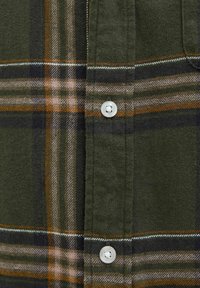 Green, black, and brown plaid fabric with two white buttons on a shirt front seam detail.