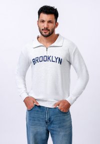 Světlě šedá mikina se čtvrtinovým zipem, s nápisem "BROOKLYN" v námořnické modři přes hruď. Texturovaná tkanina, dlouhé rukávy a žebrované manžety.