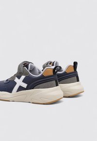 Sneakers sportivi blu navy e grigi con un design a croce bianca, accenti grigi testurizzati, linguetta imbottita e suole in gomma. Piccola etichetta di tiraggio sul retro.