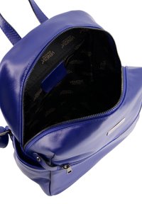 Sac à dos en cuir bleu avec une texture lisse, compartiment principal à fermeture éclair et une poche intérieure. Présente un logo argenté à l'extérieur.