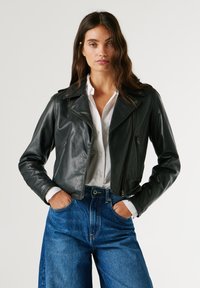 Μαύρο δερμάτινο μπουφάν μηχανής με εφαρμοστό σχέδιο, κολάρο πέτου και τσέπες με φερμουάρ, συνδυασμένο με αφράτους μπλε τζιν παντελόνες.