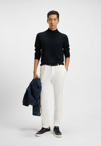 Maglione aderente nero a collo alto, pantaloni bianchi su misura, che porta una giacca blu scuro. Sneakers nere con suola bianca, design minimalista.