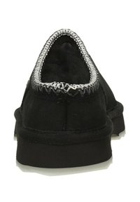 Zapatos negros sin cordones con parte superior de tela suave, que presentan un ribete plateado cosido a lo largo del cuello. La suela es plana y texturizada para mayor agarre.