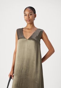 Robe sans manches en satin vert olive, présentant une texture lisse et un design fluide, avec une silhouette simple et sans embellissements.
