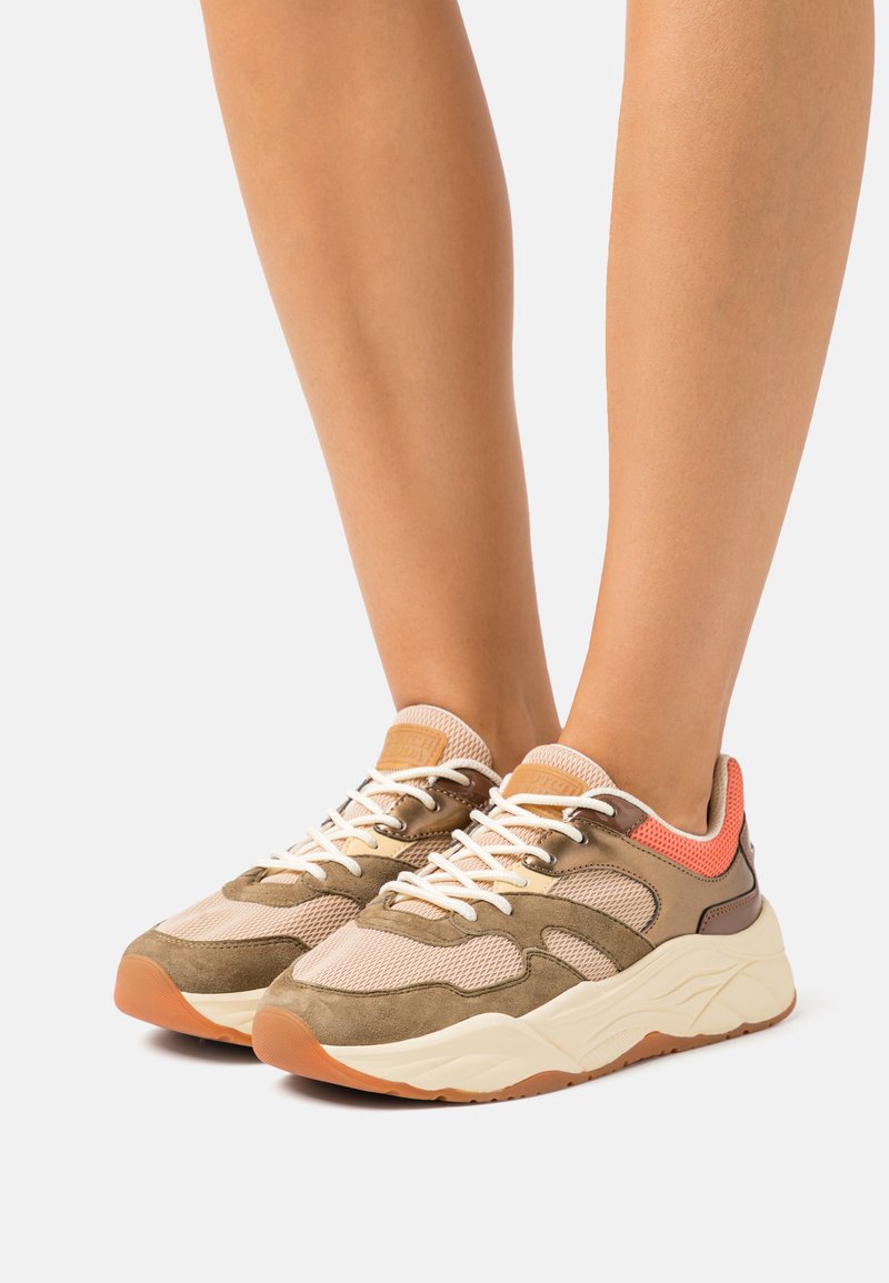 Sneakers met een bovenwerk van bruin en beige stof, netpanelen en witte veters. Heeft een gestructureerde zool en oranje accenten.