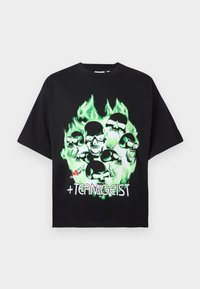 Tricou oversized negru din bumbac, cu un grafic verde al unui craniu în flăcări și textul "+TEAMGEIST" în alb pe față.