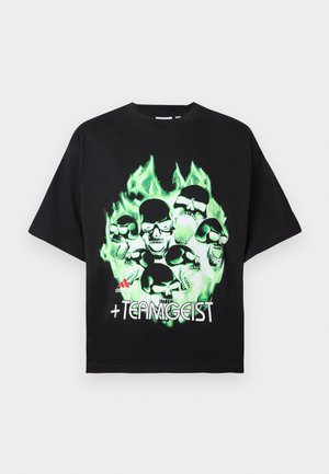 T-shirt oversized preta feita de algodão, apresentando um gráfico de um crânio verde com chamas e o texto "+TEAMGEIST" em branco na frente.