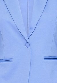 Blazer bleu clair avec une fermeture à un bouton, deux poches passepoilées et un col à revers cranté.