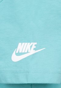 Tyrkis bomulls T-skjorte med en fremtredende hvit Nike-logo. Myk tekstur med korte ermer og rund hals.