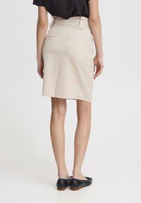 Knee-lång beige kjol med skräddarsydd passform, slät front och två bakfickor; som bärs med svarta ballerina-skor. Slät tygstruktur.