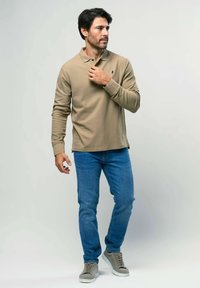 Beige pikasärgil on pika varruka, kaelus ja kolm nuppu, mis on paari pandud siniste teksade ja hallide spordijalatsitega. Üksik tekstuur ja sobiv disain.