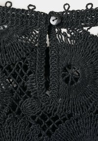 Gros plan d’un tissu au crochet noir avec des motifs géométriques et un seul bouton noir fixant deux côtés ensemble.