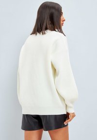 Överdimensionerad vit ribbad tröja med långa ballongärmar och bred nederkant, lagd över svarta lädershorts. Strukturerad stickad kvalitet.
