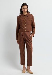 Brun skräddarsydd tvådelad outfit med en croppad kavaj med krage och guldknappar samt matchande högmidjade byxor.