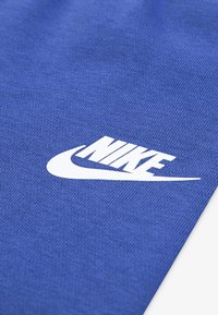 Plava tkanina s teksturiranom površinom koja prikazuje istaknuti bijeli Nike logo i dizajn swoosh.