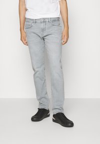 Jeans in denim grigio con vestibilità dritta, cinque tasche e dettagli di cucitura sottili, abbinati a sneakers nere con accenti rossi e bianchi.