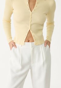 Lichtgele geribde cardigan met een V-hals en meerdere knopen, gecombineerd met witte tailored broek met zijzakken en een soepele textuur.