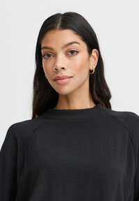 Maglietta nera a maniche lunghe con scollo rotondo e maniche raglan, realizzata in tessuto leggero con una sottile texture. Accentata da hardware minimale.