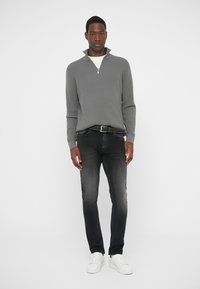 Gray ribbed sweater with a half-zip collar, paired with dark gray jeans and white sneakers. Flat textured fabric, fitted design.