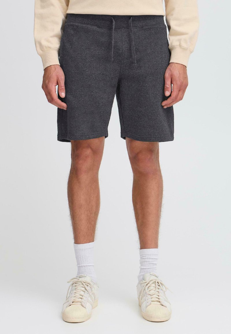 Shorts de sport gris foncé, mi-cuisse, en tissu doux avec une taille élastique et un cordon de serrage. Offre une coupe décontractée et sans poches visibles.