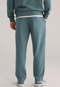 Tirkizne sportske hlače opuštenog kroja, izrađene od mekanog materijala. Imaju bočne džepove i rebraste manžete. Uparene s tenisicama s uzorkom.