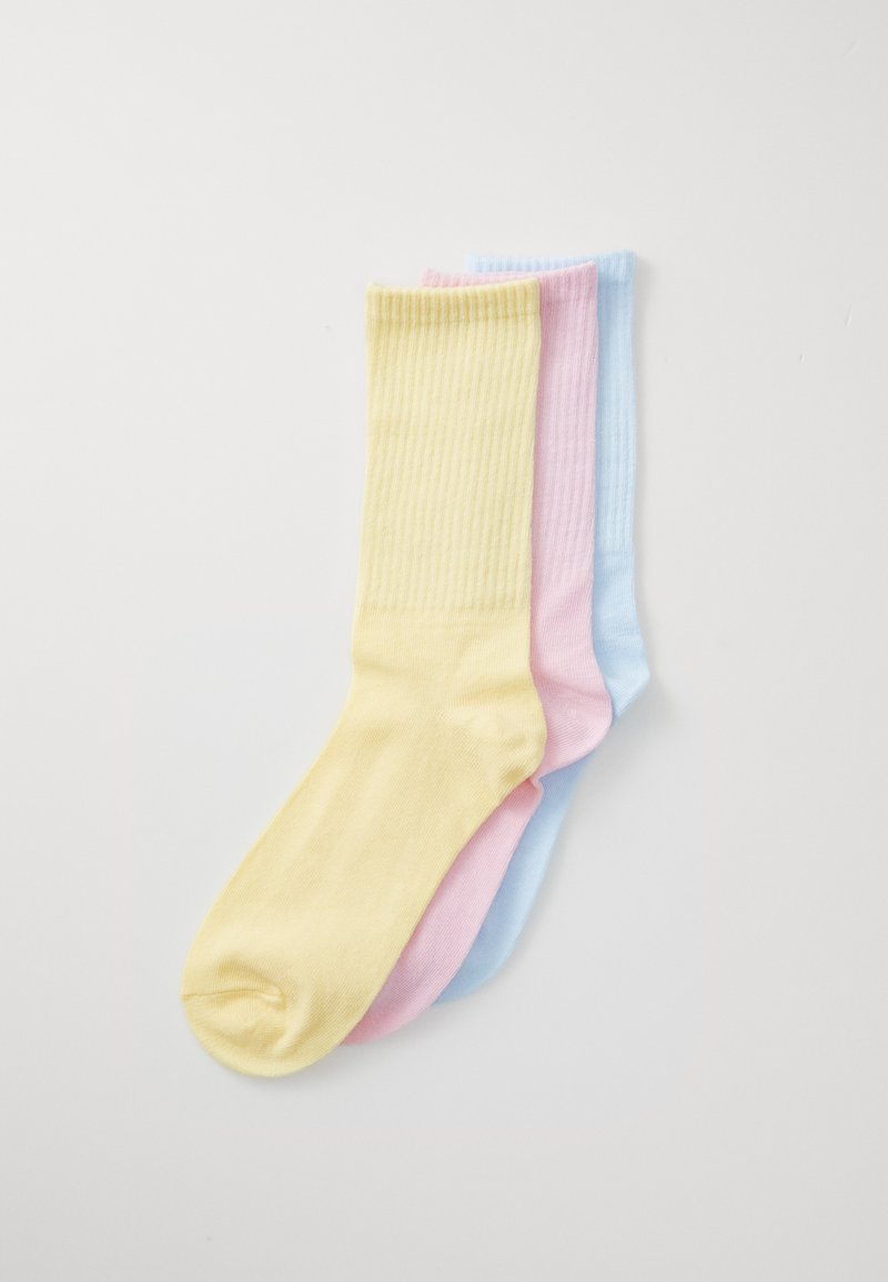 Troje rebrované ponožky v žltej, ružovej a svetlomodrej farbe. Každá ponožka má jednoliatu farbu a jemnú textíliu, bez vzorov alebo kovových detailov.