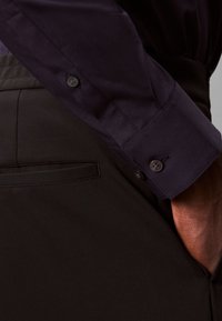Navy shirt with buttoned cuff, paired with black pants featuring a back pocket. Fabric appears smooth with tailored fit details.