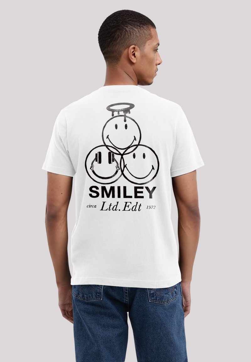 White cotton t-shirt featuring a graphic of three smiley faces in black, labeled "SMILEY," with a halo and headphones design.
