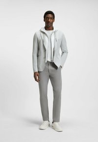 Blazer gris clair avec un sweat à capuche en dessous, associé à un pantalon gris clair et des baskets blanches. Tissu lisse avec un design moderne.