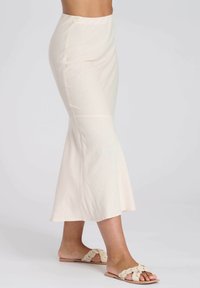 Een crèmekleurige flared midi rok van zachte stof met een gladde textuur. Gecombineerd met beige instapsandalen met een geknoopt ontwerp.