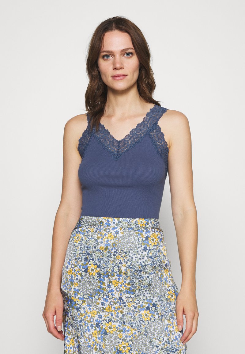 Marinblå ribbestrikket tanktop med blondekant på skuldrene og halsen, kombinert med et blomstermønstrete skjørt med blå og gule detaljer.