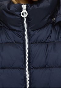 Marineblaue Steppjacke mit hohem Kragen, weißem Reißverschluss und gesteppter Textur mit auffälligen Nahtdetails.