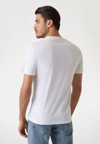 Balta trumpa rankovė t-shirt su klasikiniu apvaliu iškirpimu, lygiu paviršiumi, prigludusia forma ir švariu, minimalistiniu stiliumi, derinama su džinsais.