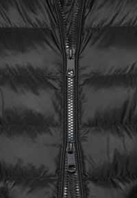 Chaqueta de plumas negra con cierre delantero, patrón acolchado horizontal, textura suave y un tirador de cremallera con marca.