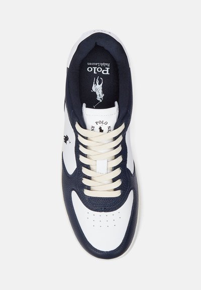 Valge ja tumesinine sportking, millel on tekstureeritud disain, kreemilised paelad, augustatud varbadetailid ja silmapaistev kaubamärgi logo keele sees.