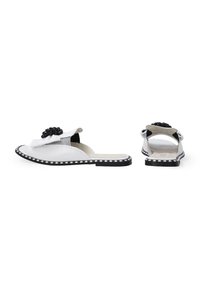 Witte instapsandalen met een gestructureerde, bloemige zwarte acccent en zilveren details. Voorzien van een platte zwarte zool met decoratieve stiksels.
