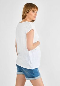 Biely top s krátkymi rukávmi a voľným strihom, s oblým lemom a jemnou textúrou, skombinovaný s nohavicami z denimu s vyhrnutými okrajmi.