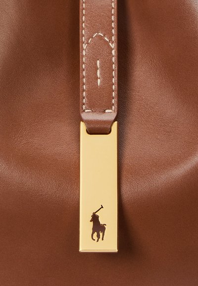 Ruda odinė rankinė su auksiniu užsegimu, kuriame pavaizduotas polo žaidėjas ir arklys, detalus siuvimas ir lygus paviršius.